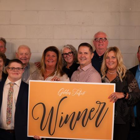 Group of auction winners holding a large gold sign that says “winner”